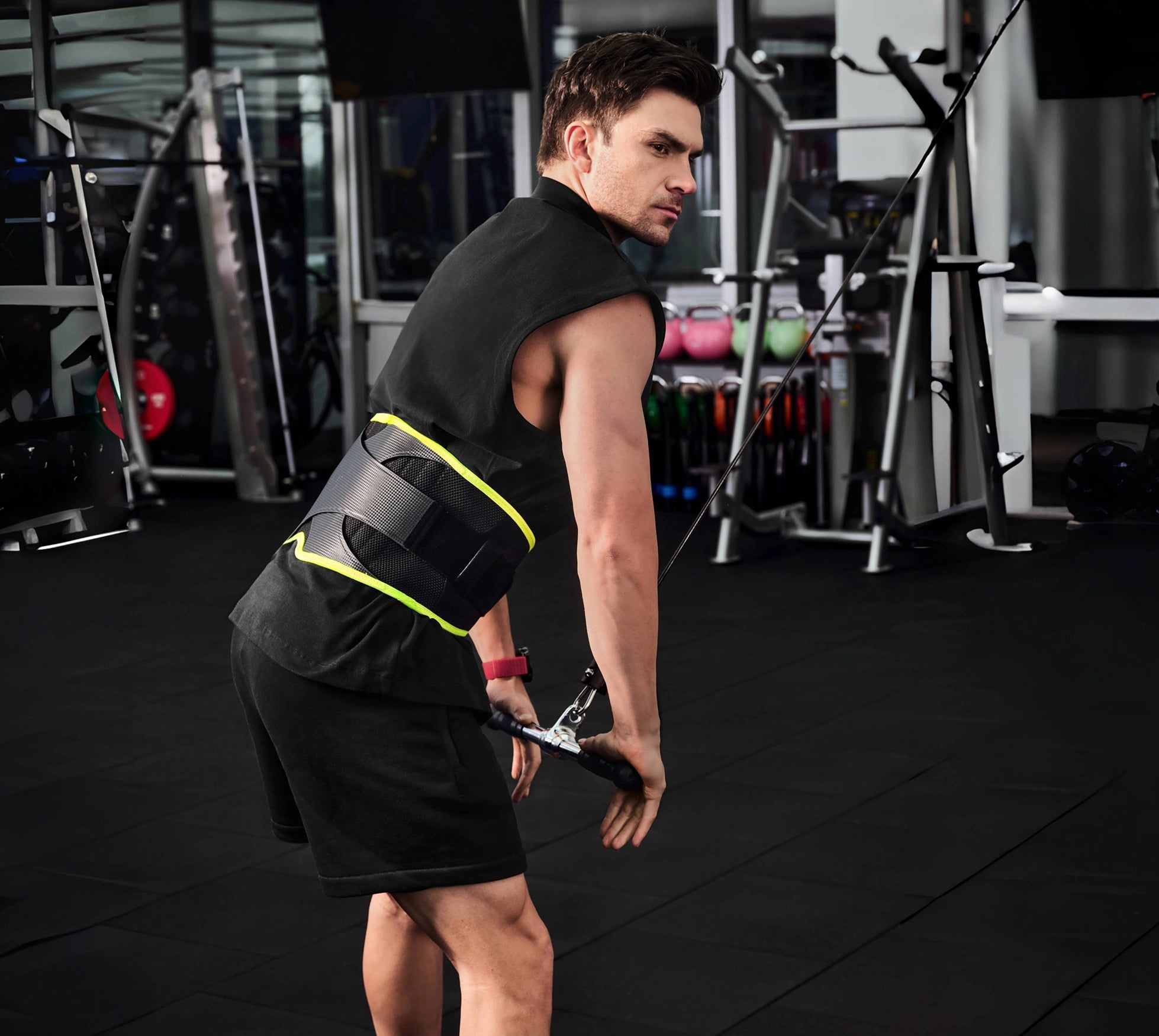 Man wearing a black back brace with yellow accents in a gym setting